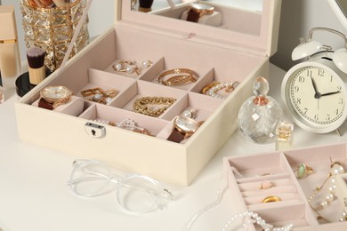 Photo of Jewelry boxes with many different accessories, perfumes and alarm clock on white table