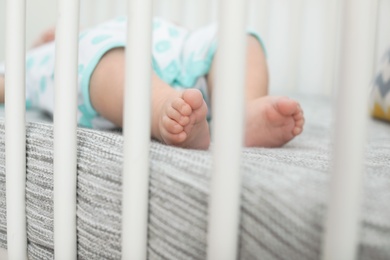 Photo of Little baby lying in crib, closeup of legs