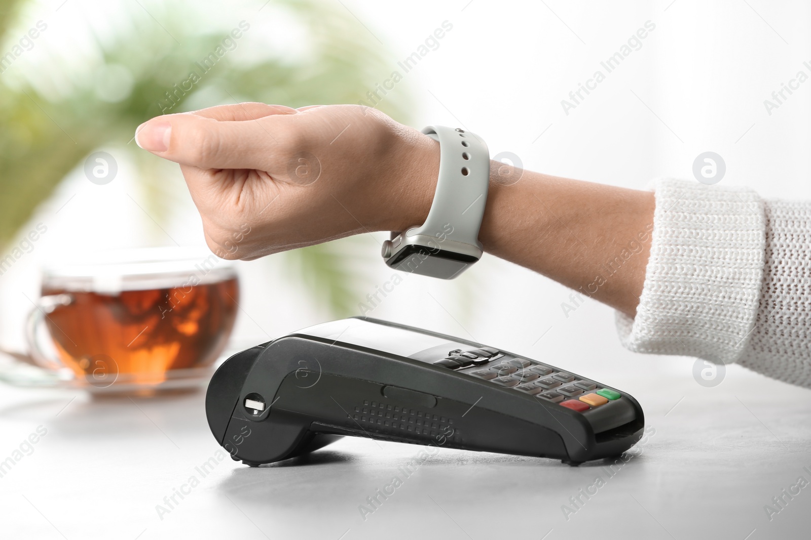 Photo of Woman using terminal for contactless payment with smart watch at table, closeup