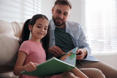 Photo of Little girl with father reading fairy tale in living room