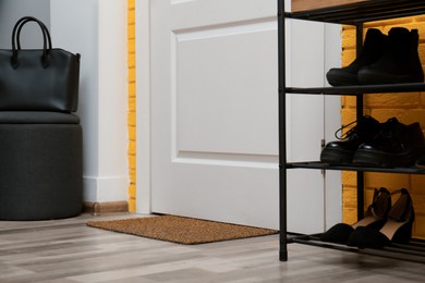 Photo of Door mat and shelving unit with shoes in hallway