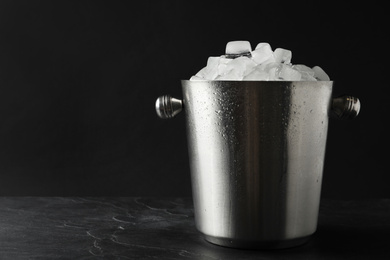 Photo of Metal bucket with ice cubes on table. Space for text