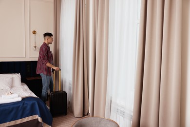 Photo of Handsome man with suitcase near window in hotel room