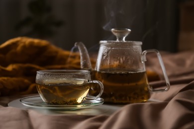 Tray with cup of hot tea and teapot on bed