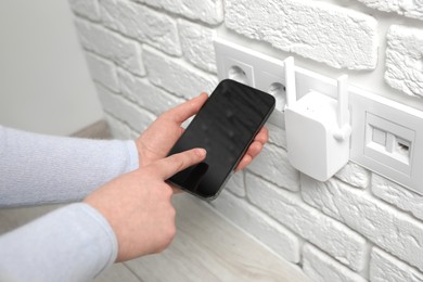 Photo of Woman using smartphone for wireless Wi-Fi repeater indoors, closeup