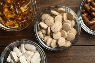 Different dietary supplements in glass bowls on wooden table, flat lay