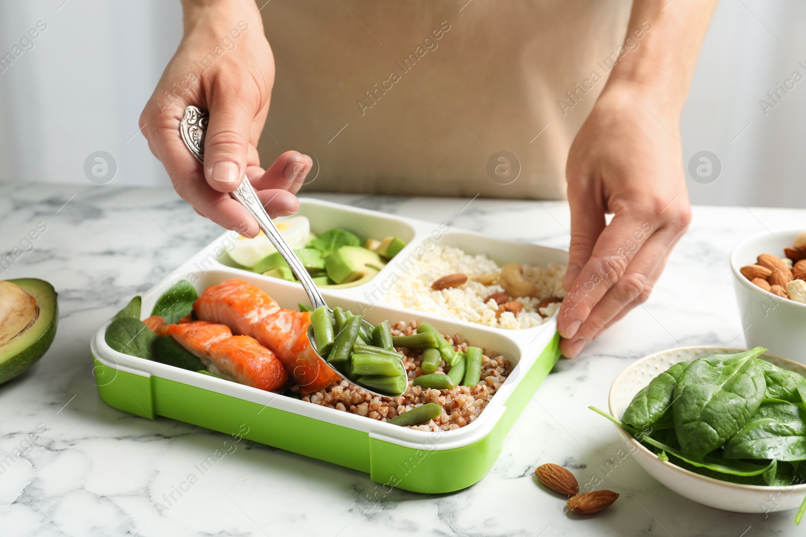 Photo of Woman putting natural protein food into container on marble table, closeup