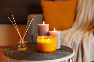 Photo of Burning candles and reed air freshener on table indoors. Cosy atmosphere