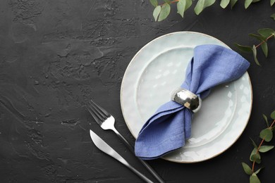 Stylish setting with cutlery, eucalyptus branches, napkin and plate on dark textured table, flat lay. Space for text