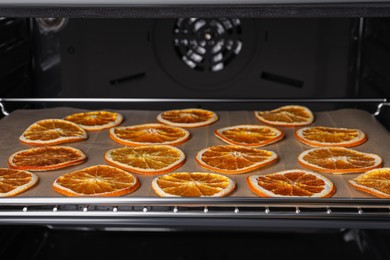 Photo of Many dry orange slices on parchment paper in oven