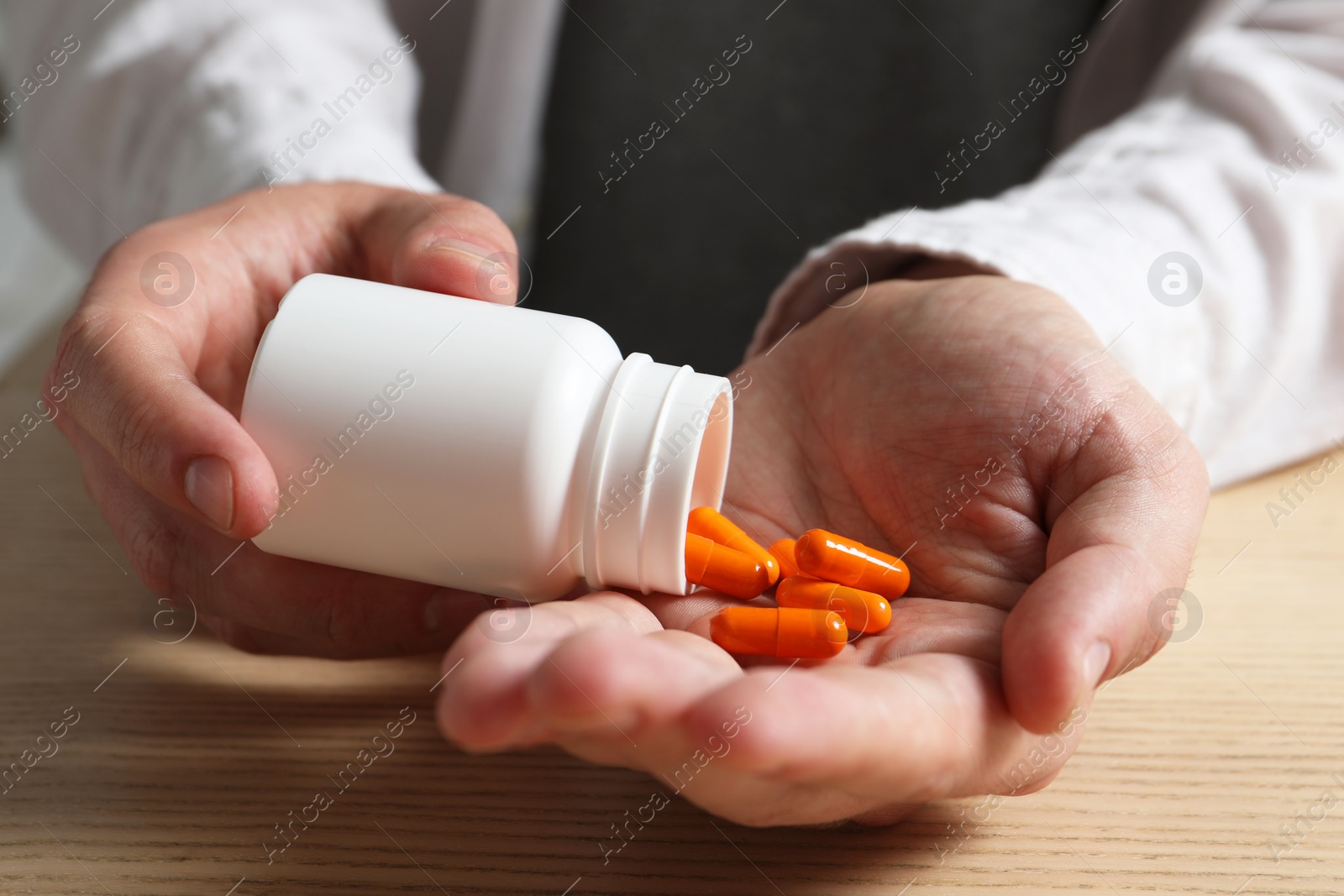 Photo of Man pouring pills from bottle at wooden table, closeup