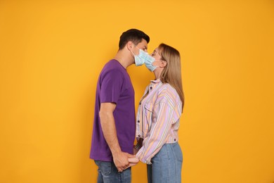 Photo of Couple in medical masks trying to kiss on yellow background