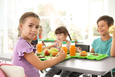Photo of Children sitting at table and eating healthy food during break at school