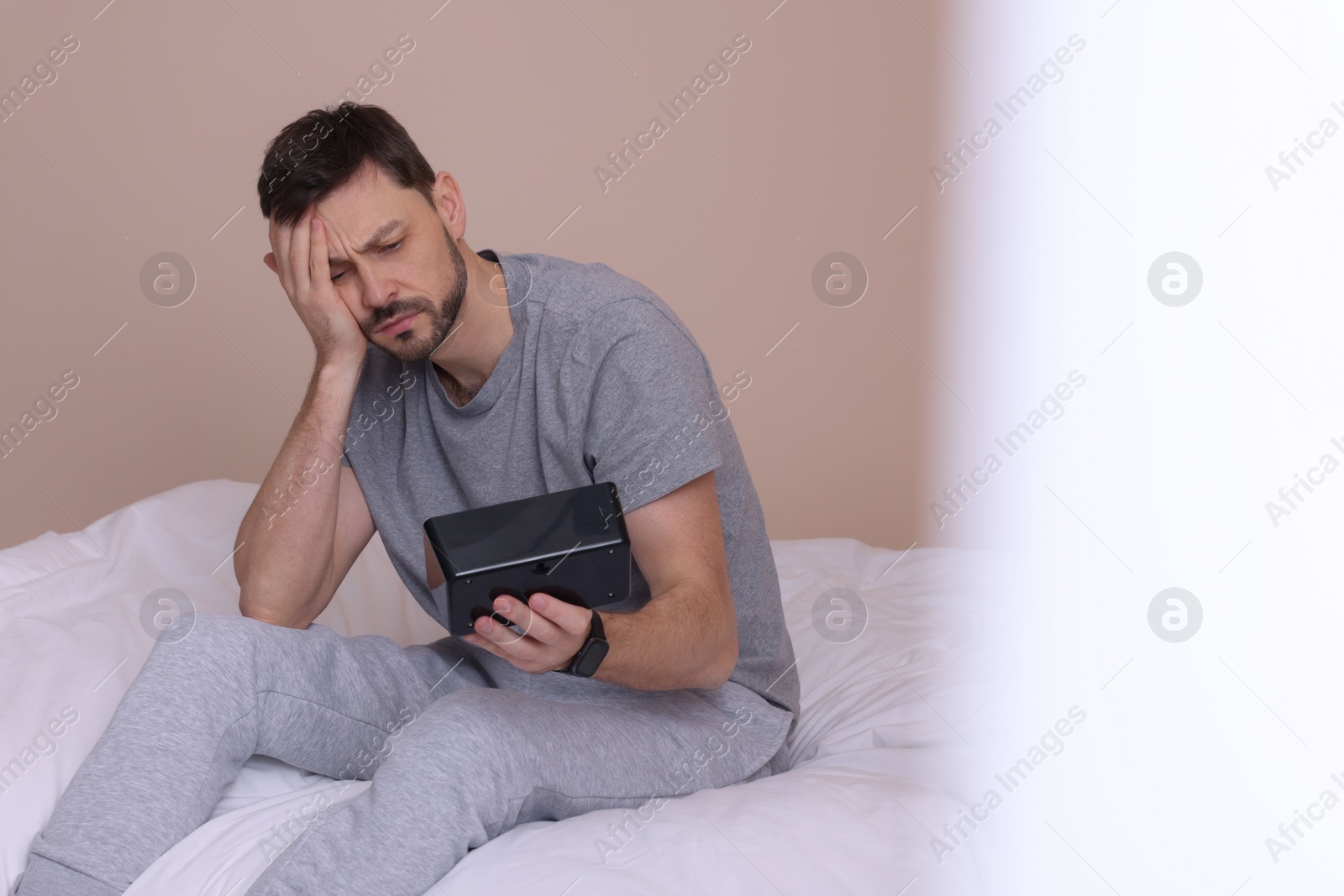 Photo of Sleepy man with clock in bed at home