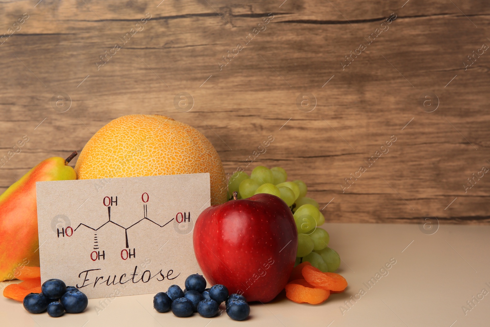 Photo of Card with word Fructose, delicious ripe fruits, blueberries and dried apricots on beige table, space for text