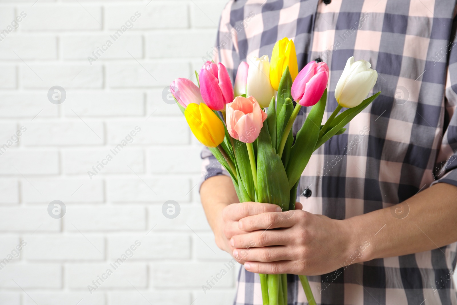 Photo of Man holding bouquet of beautiful spring tulips near brick wall, closeup with space for text. International Women's Day