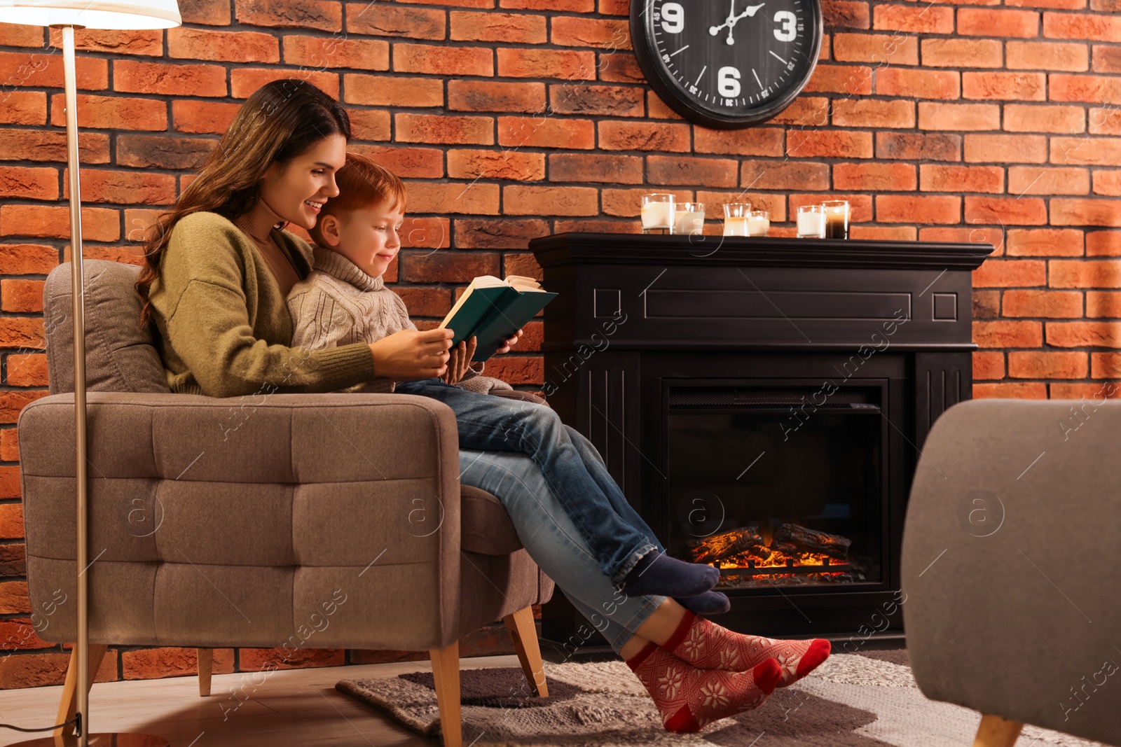 Photo of Happy mother and son reading book together near fireplace at home