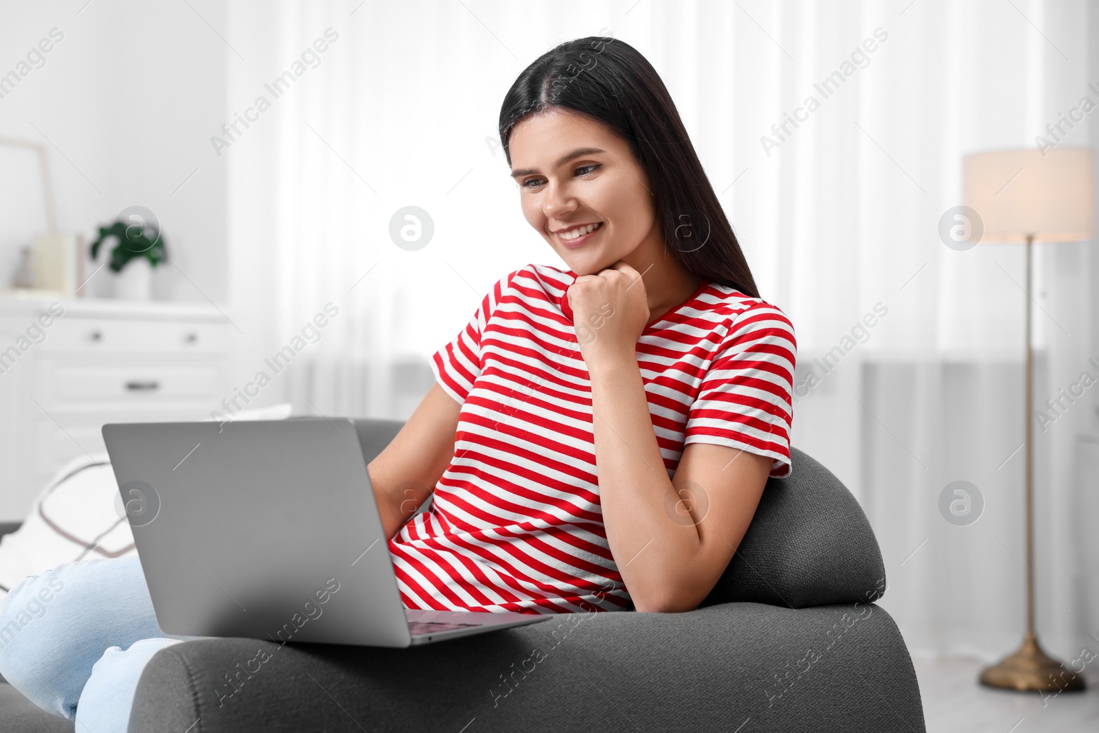 Photo of Happy young woman having video chat via laptop on sofa in living room