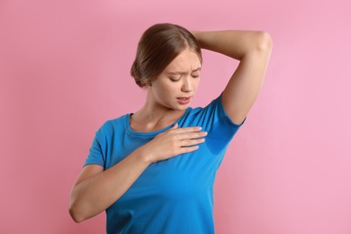 Young woman with sweat stain on her clothes against pink background. Using deodorant