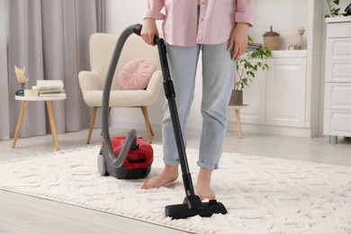 Woman cleaning carpet with vacuum cleaner at home, closeup