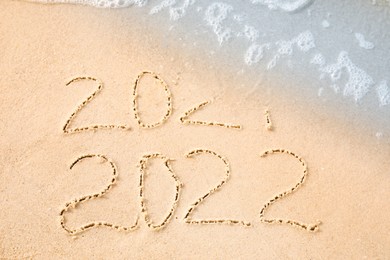 Photo of Dates written on sandy beach. 2021 washed by sea wave as New 2022 Year coming, above view