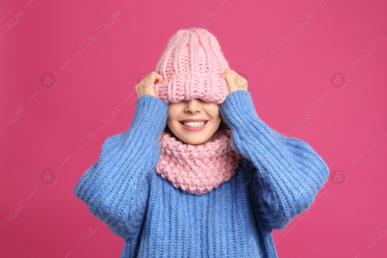 Photo of Young woman wearing warm sweater, snood and hat on crimson background. Winter season
