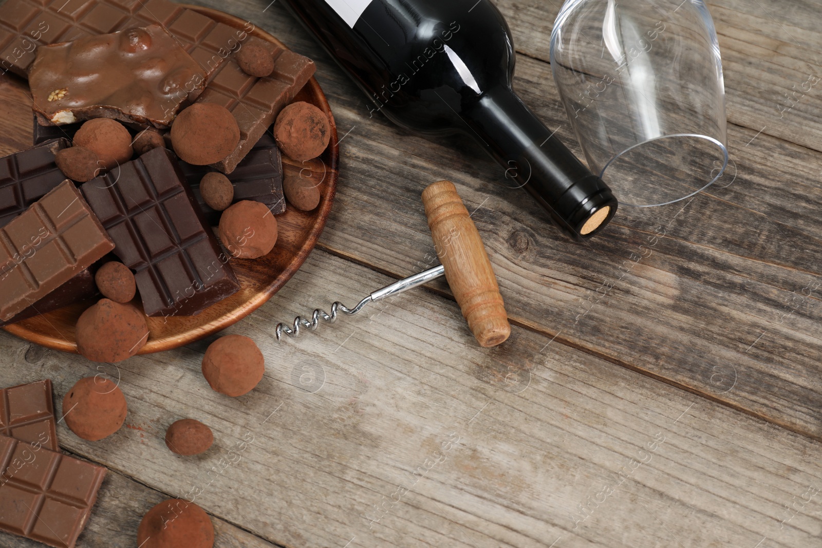 Photo of Bottle of red wine, glass, chocolate sweets and corkscrew on wooden table, above view. Space for text