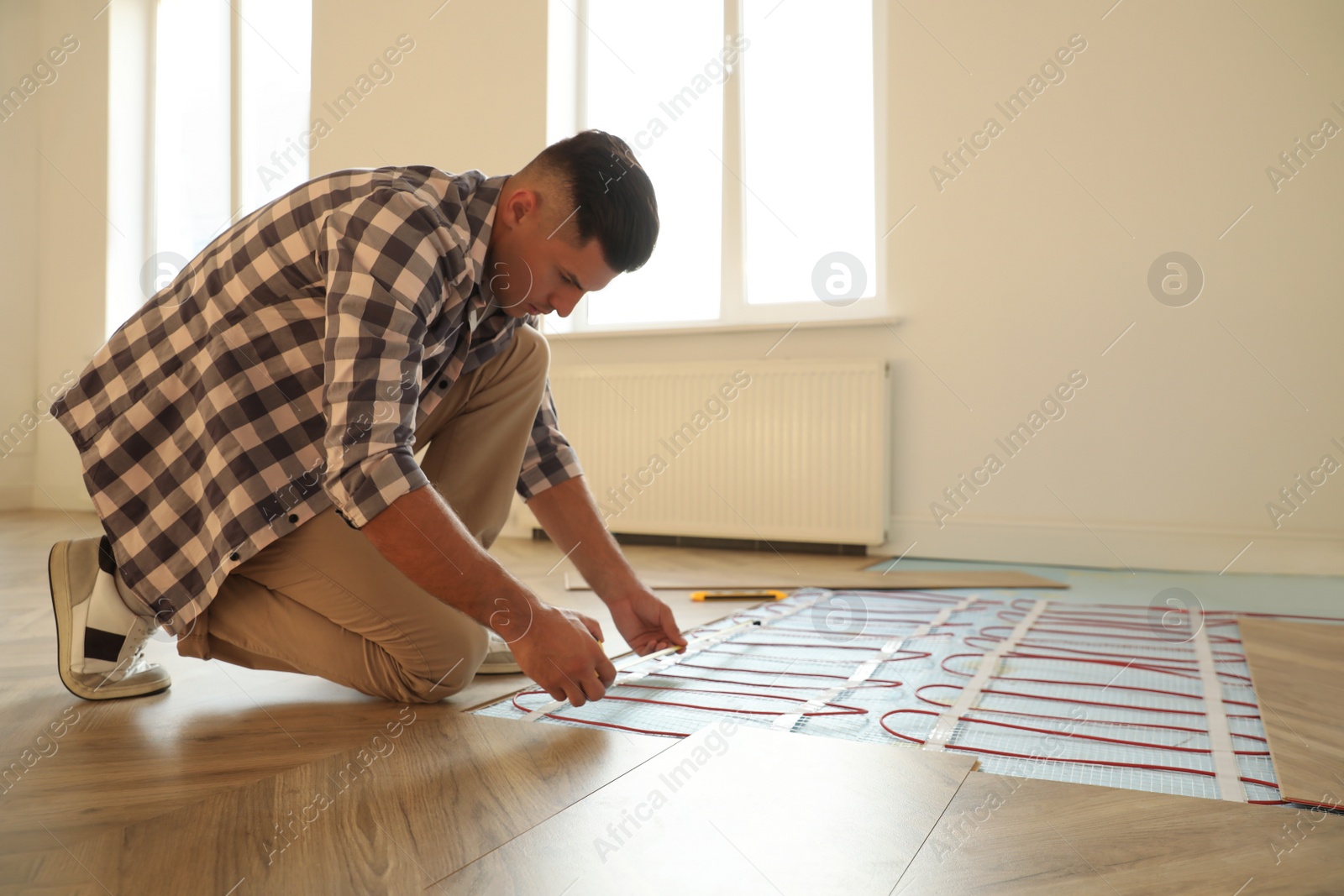 Photo of Professional worker installing electric underfloor heating system indoors