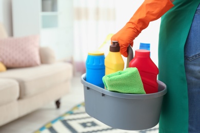 Woman with basin of detergents in living room, closeup. Cleaning service