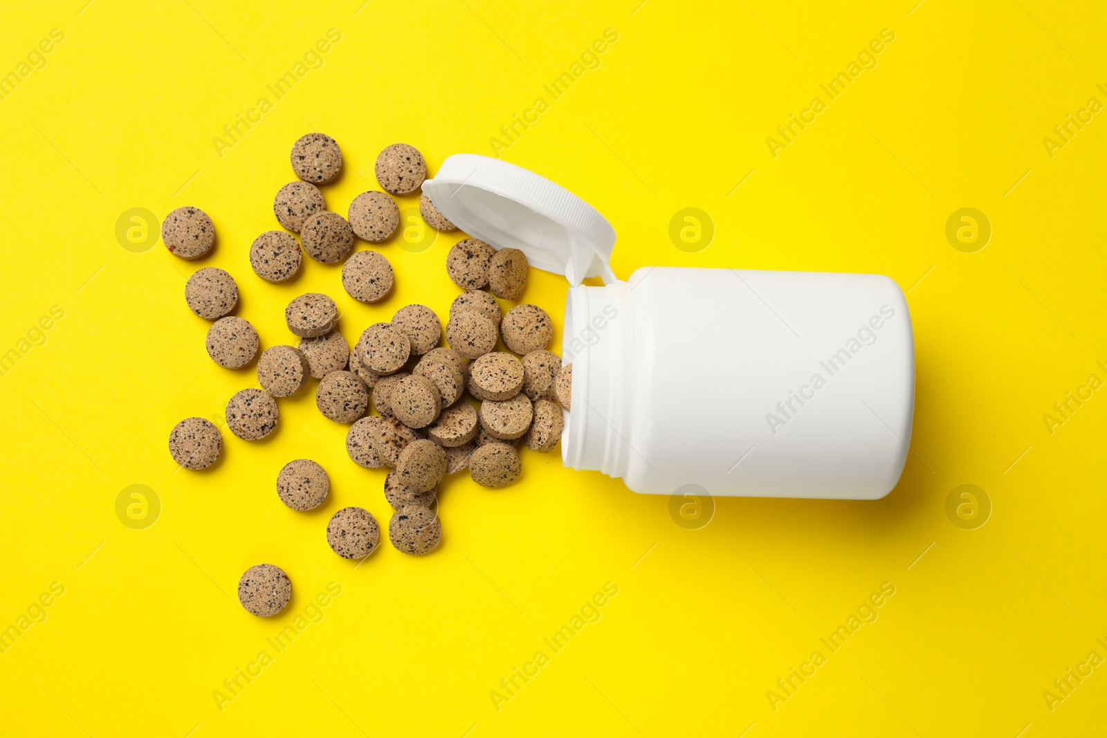 Photo of Vitamin pills and bottle on yellow background, top view