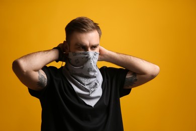 Young man covering his face with bandana on yellow background