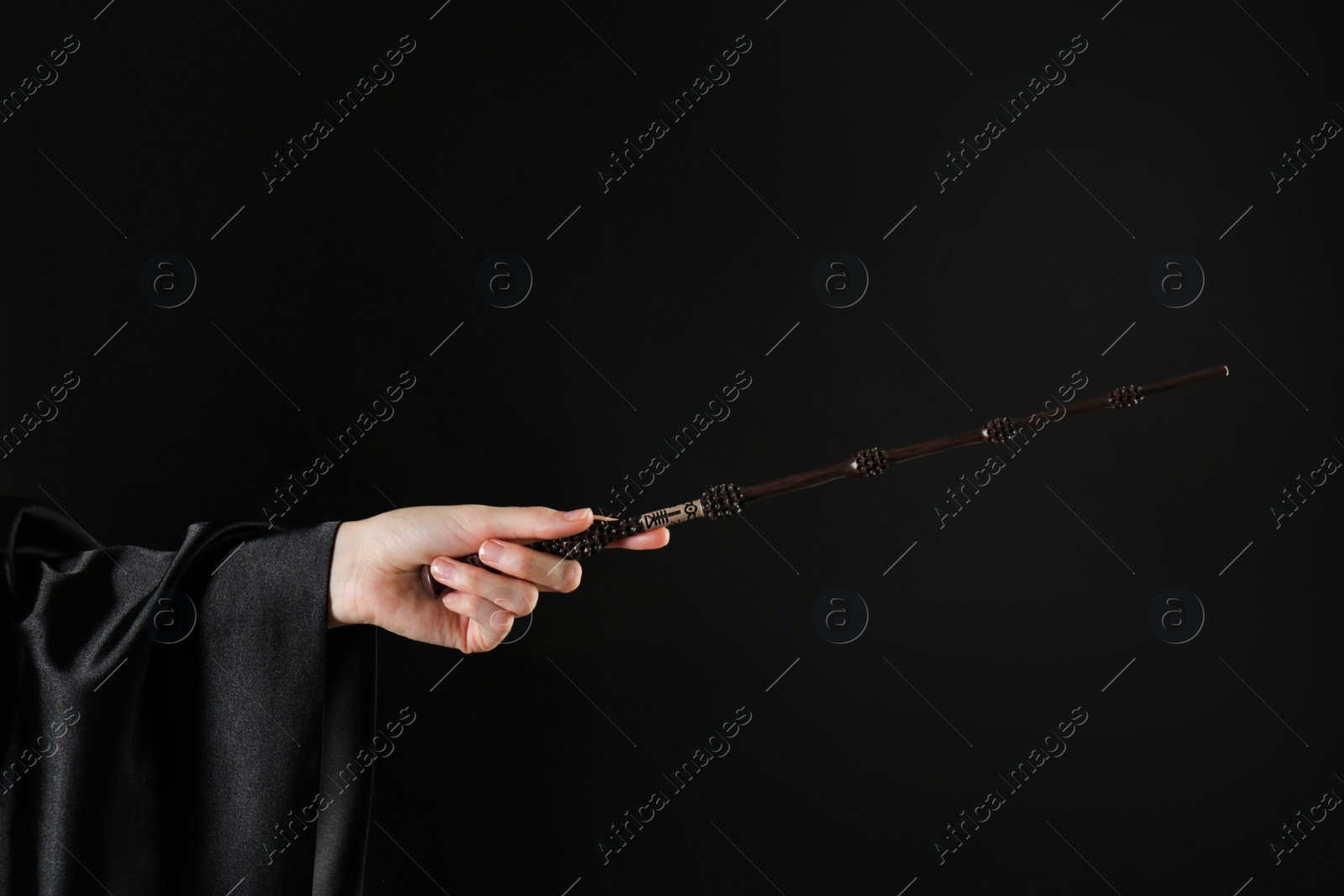 Photo of Wizard holding magic wand on black background, closeup