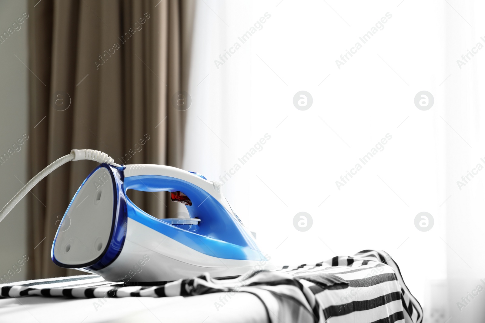 Photo of Modern electric iron on board indoors, space for text. Household appliance