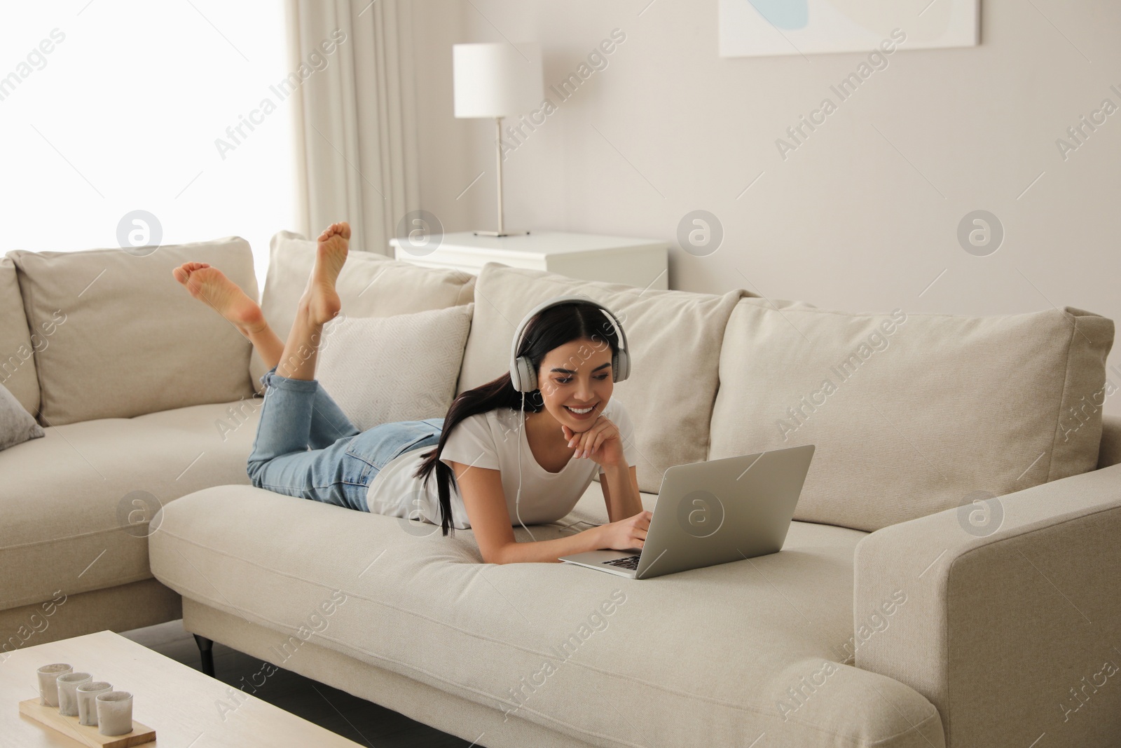 Photo of Woman with laptop and headphones lying on sofa at home