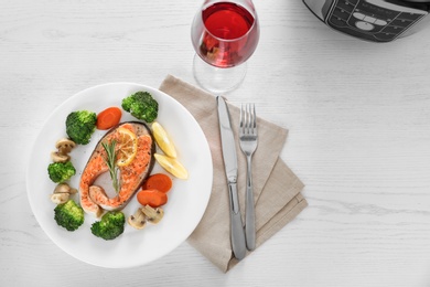 Photo of Plate with salmon steak and garnish prepared in multi cooker on table, flat lay