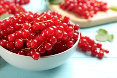 Photo of Delicious red currants in bowl on light blue table, closeup
