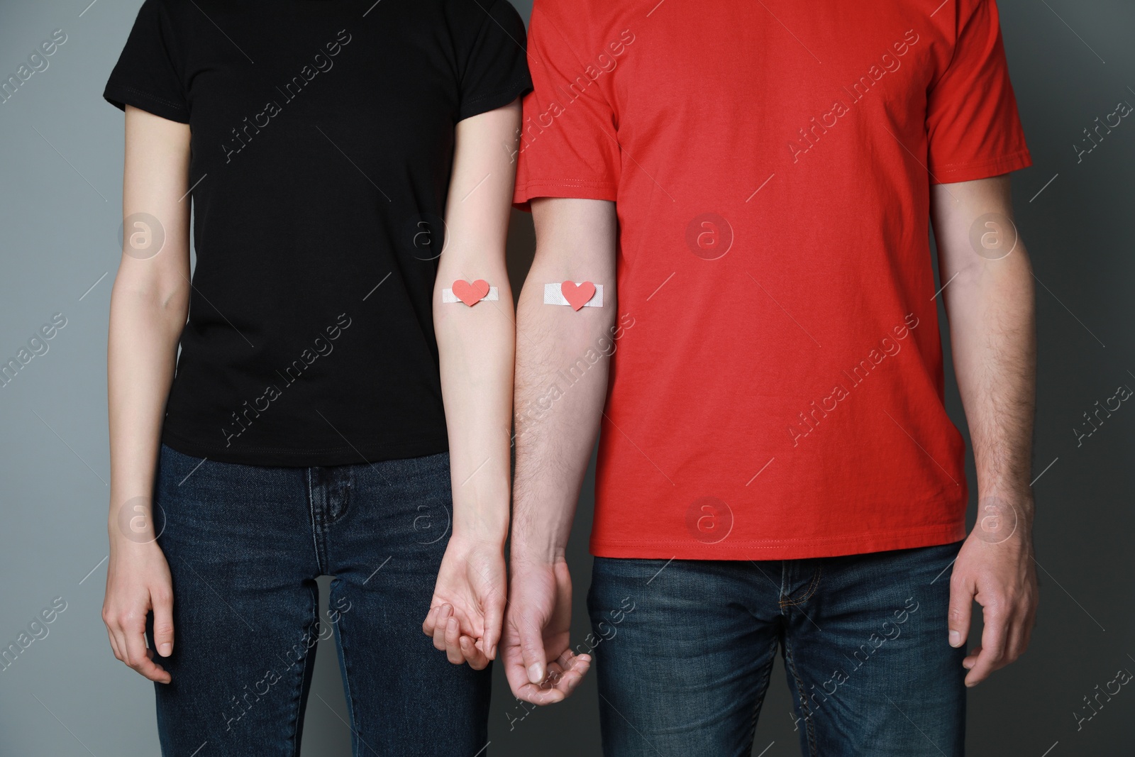Photo of Blood donation concept. Couple with adhesive plasters on arms against grey background, closeup