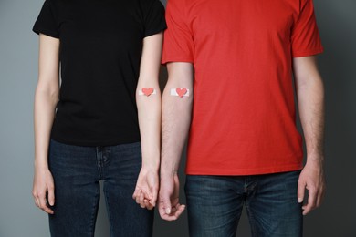 Photo of Blood donation concept. Couple with adhesive plasters on arms against grey background, closeup