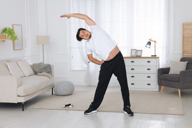 Photo of Overweight man stretching near sofa in living room