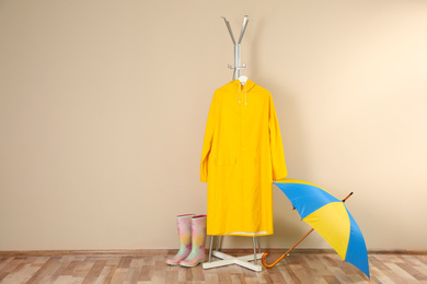 Photo of Umbrella, rain coat and rubber boots near beige wall. Space for text