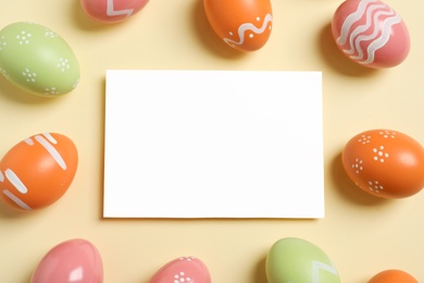 Flat lay composition of painted Easter eggs and blank card on color background, space for text