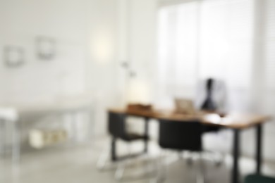 Photo of Blurred view of modern medical office with doctor's workplace and examination table. Interior design