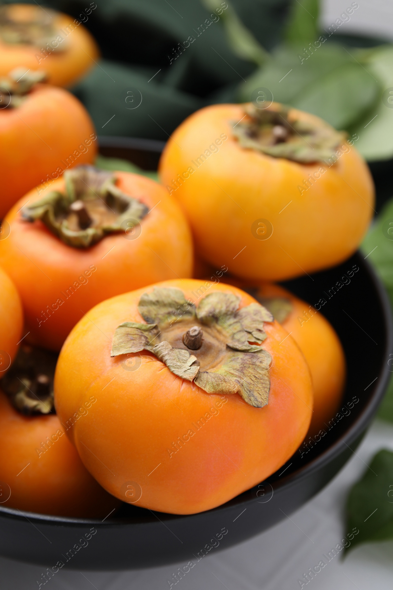 Photo of Bowl with delicious ripe juicy persimmons on white table, closeup