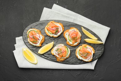 Photo of Tasty canapes with salmon, cucumber, radish and cream cheese on black table, top view