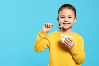 Photo of Girl eating tasty yogurt on light blue background, space for text