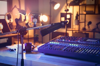 Photo of Microphone near table with professional mixing console in radio studio