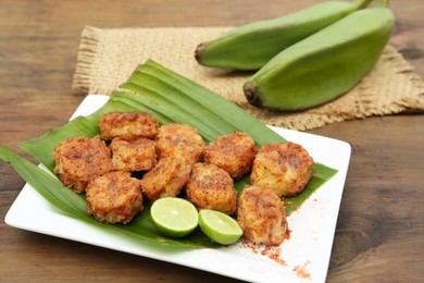 Photo of Delicious fried bananas, fresh fruits and cut limes on wooden table