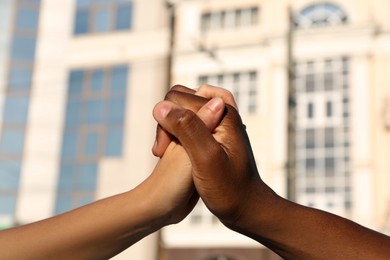 Woman and African American man clasping hands on city street, closeup