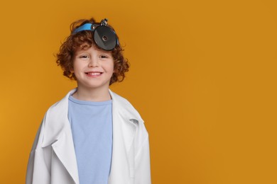 Photo of Little boy in medical uniform with head mirror on yellow background. Space for text