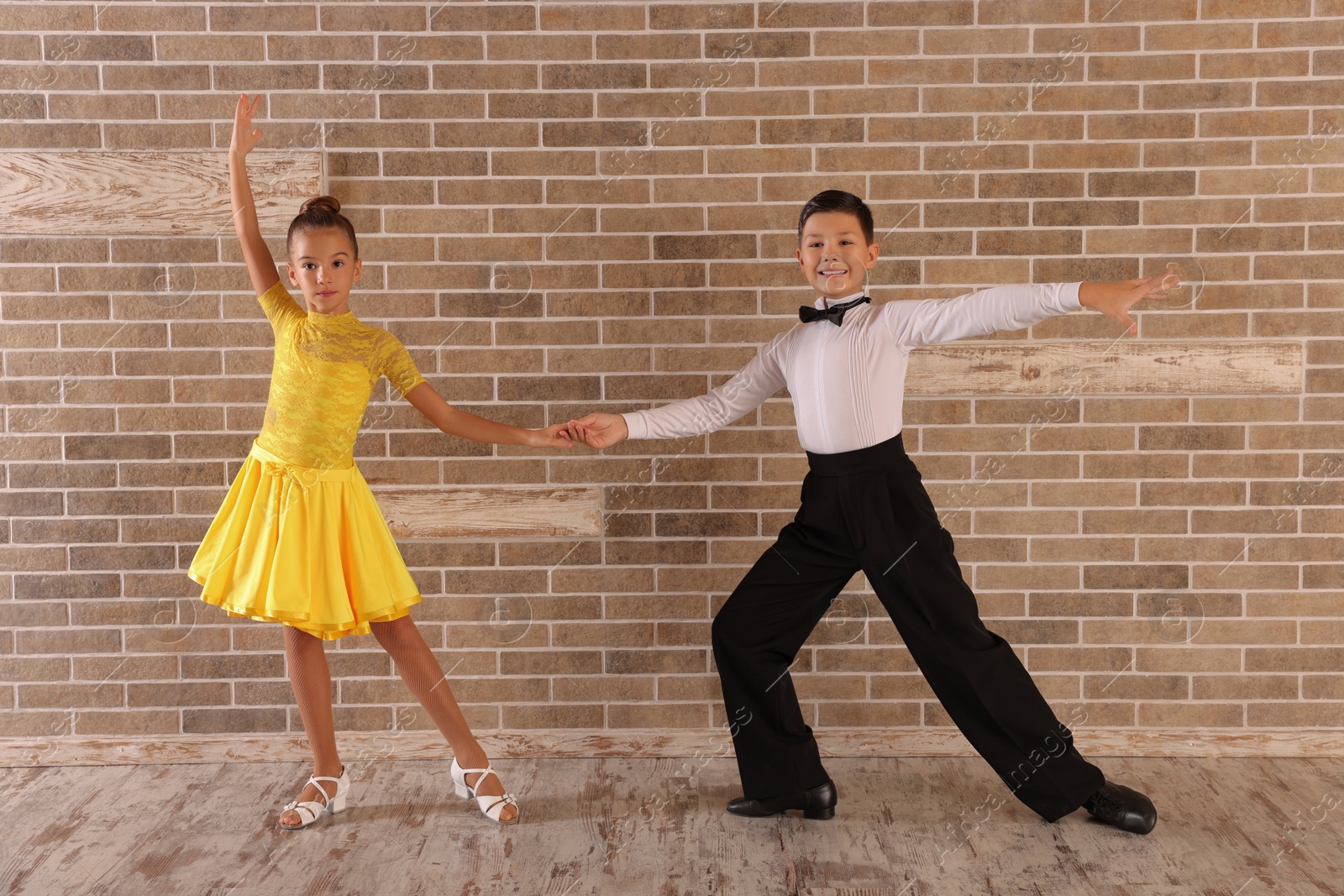 Photo of Beautifully dressed couple of kids dancing together near brick wall indoors